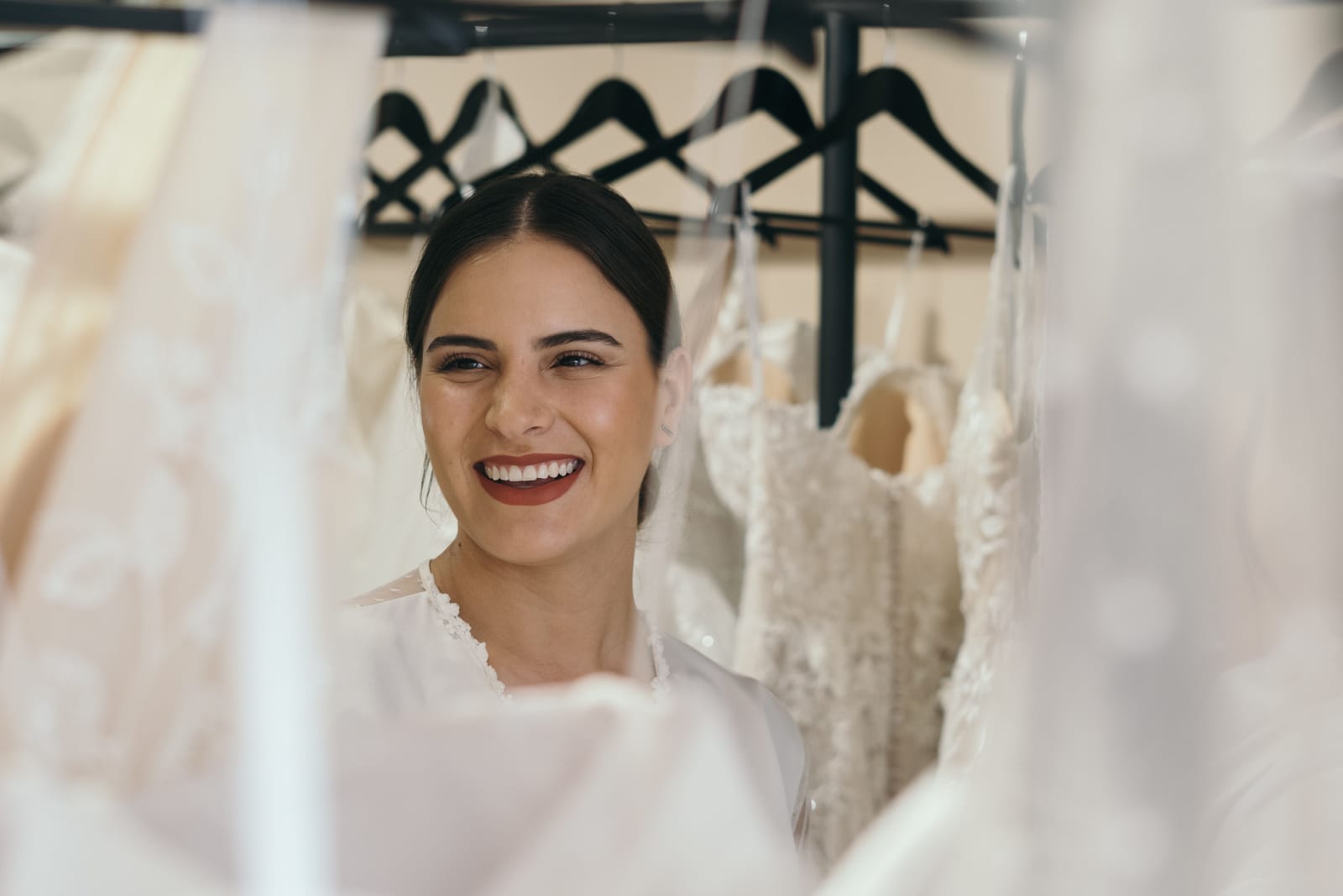 A bride smiling between racks of wedding gowns.